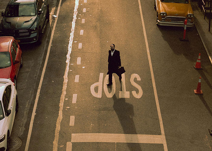Man crossing street on stop sign area with cars parked, illustrating risks of driving over the speed limit.