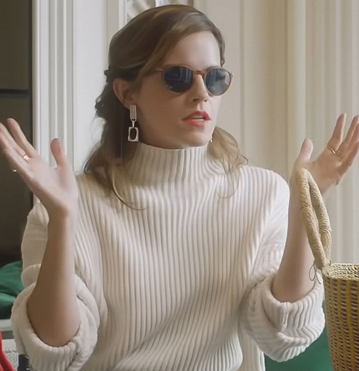 Woman wearing sunglasses and a white ribbed sweater gesturing indoors, related to Emma Watson wears see-through dress on a hike.