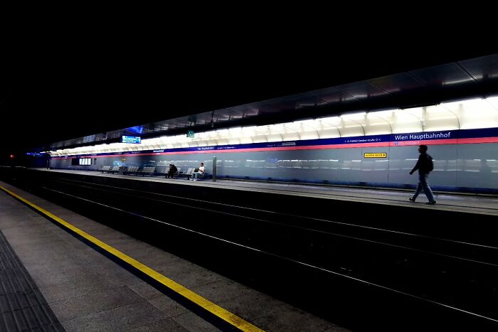 Street scene at a dimly lit train station with people waiting and walking, capturing unseen unposed moments by a photographer.