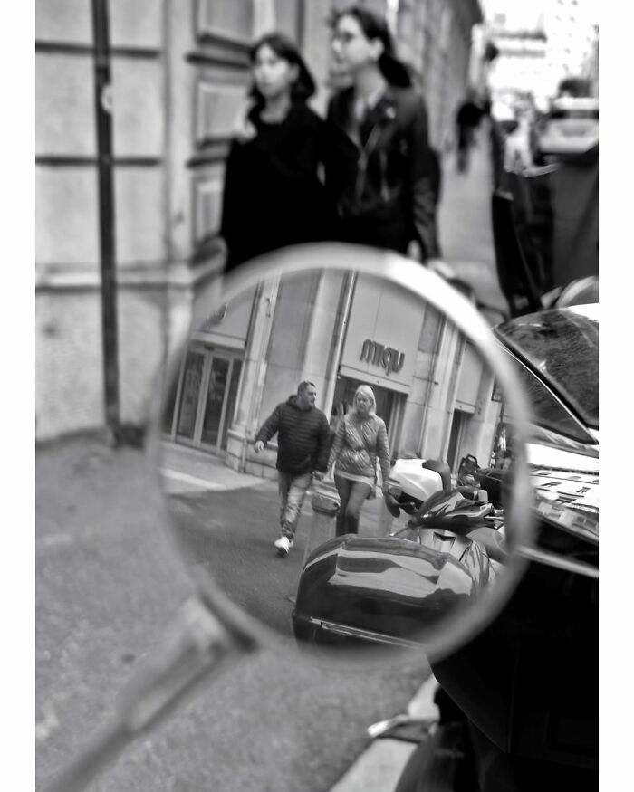 Street scene captured through a mirror showing two people walking, highlighting unseen, unposed moments on the streets by a photographer.