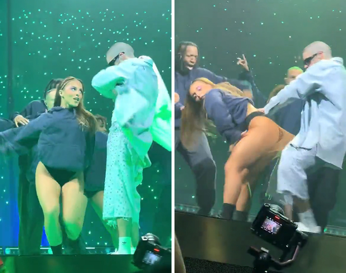 Female performer in a wardrobe malfunction moment on stage with backup dancers under green lighting.