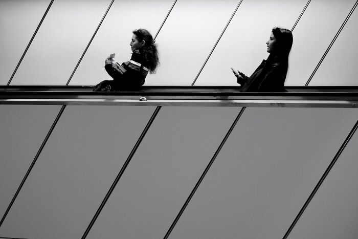Black and white photo of two women on escalator, capturing unseen, unposed moments on the streets by a photographer.