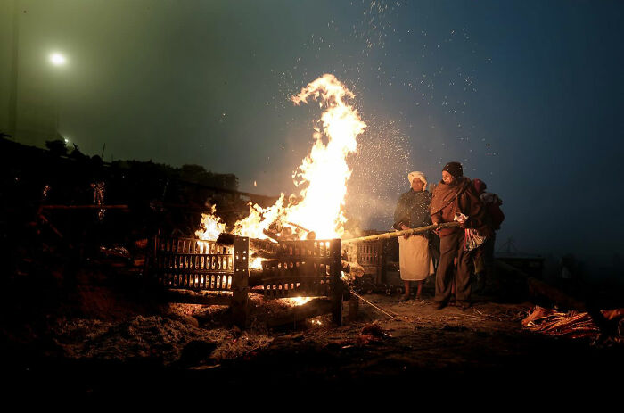 Two people tending a large fire outdoors at night, capturing candid everyday moments from Asia by photographer Gil Kreslavsky.