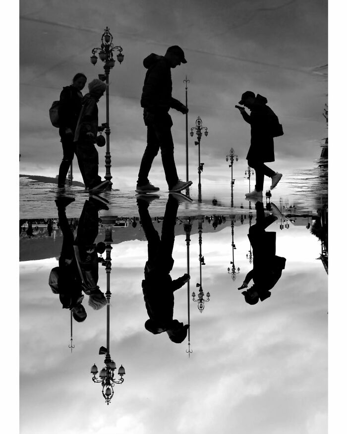 Silhouettes of people walking on wet streets, capturing unseen unposed moments reflected in puddles.