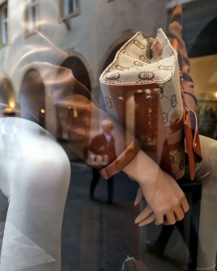 Reflection of a pedestrian walking past a mannequin holding a designer bag, capturing life’s unseen unposed moments on the streets.