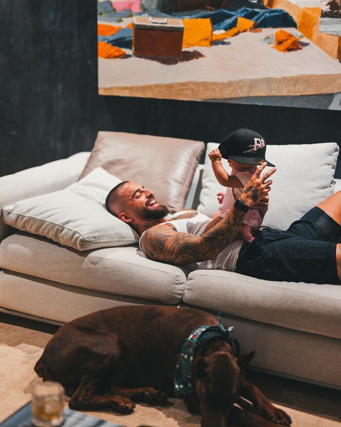 Tattooed singer relaxing on a couch with a baby, illustrating a personal moment before abruptly stopping concert over irresponsible mom. Tattooed singer relaxing on a couch with a baby, illustrating a personal moment before abruptly stopping concert over irresponsible mom.