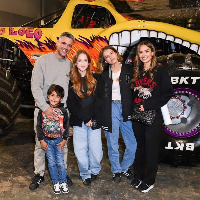 Jessica Alba smiling with family near a large monster truck, showcasing her stunning bikini body appearance.