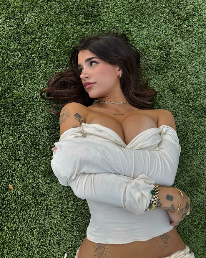Young woman with tattoos lying on grass, wearing off-shoulder white top, representing L&rsquo;Or&eacute;al controversial hiring defense.
