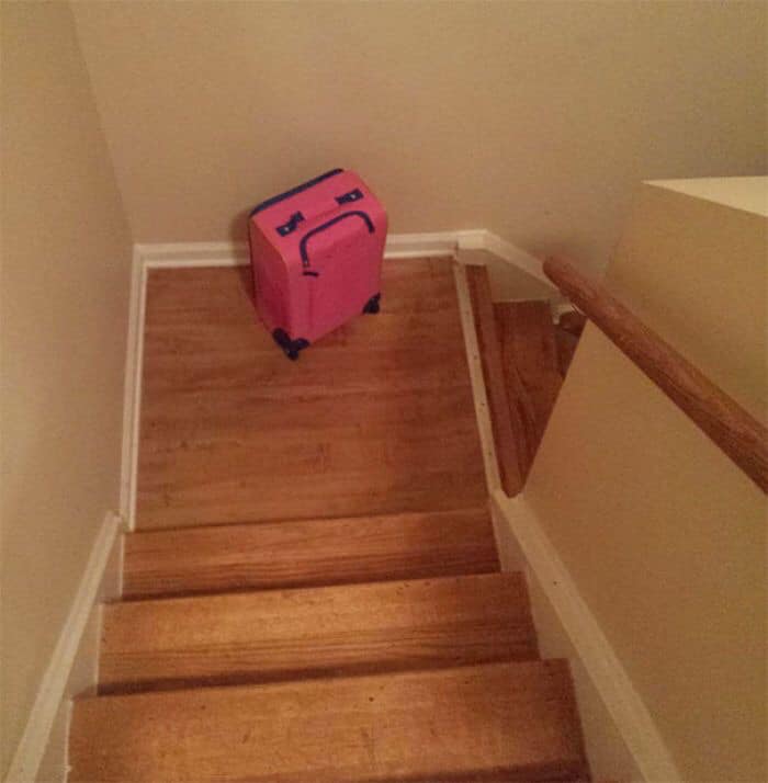Pink suitcase with drawn sad face at the bottom of wooden stairs, illustrating random objects that look like faces.