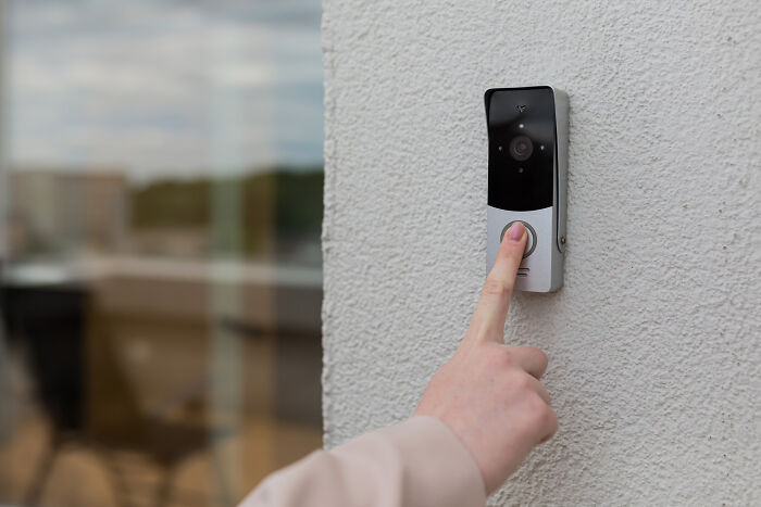 Person pressing a video doorbell button on a white wall, capturing eerie sounds heard by people at night.