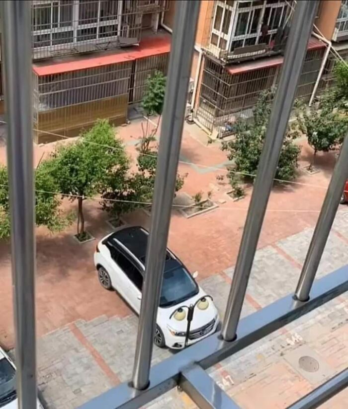 White car with stickers on the hood resembling eyes, creating a random object that looks like a face in a parking lot.