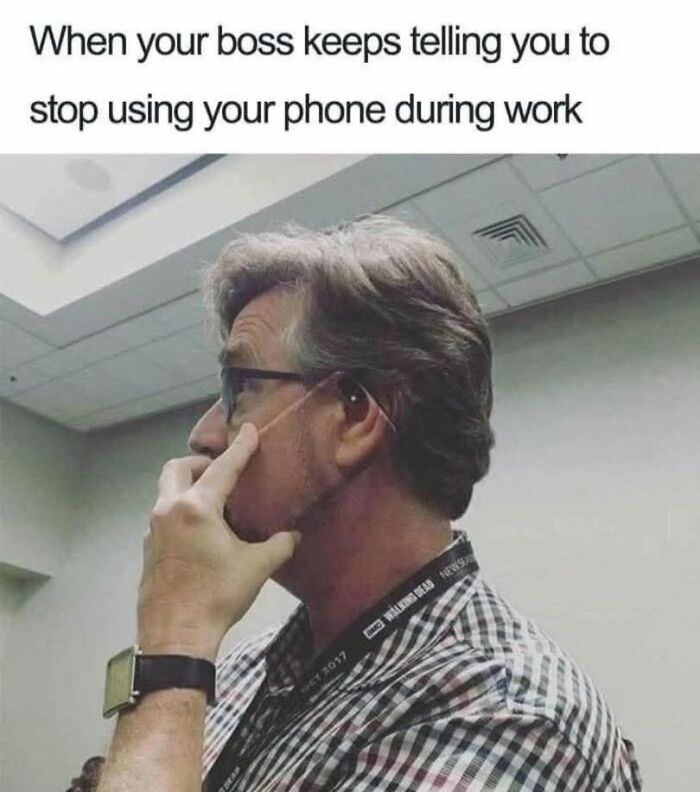 Man wearing glasses and a plaid shirt pretending to use his finger as a phone during work in a humorous work meme.