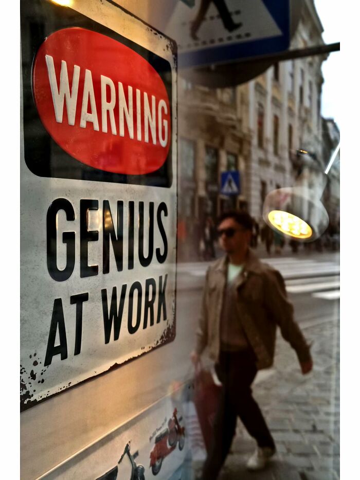Street photographer captures unseen unposed moments reflecting a warning genius sign with a pedestrian walking by.