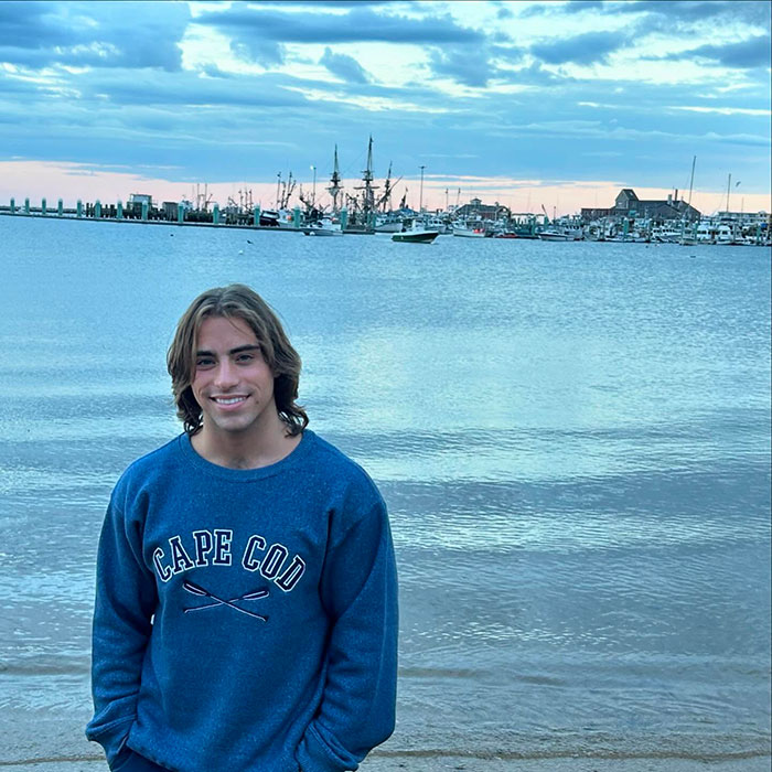 Young man standing by the water at sunset, wearing a blue Cape Cod sweatshirt, related to Chase Filandro news.