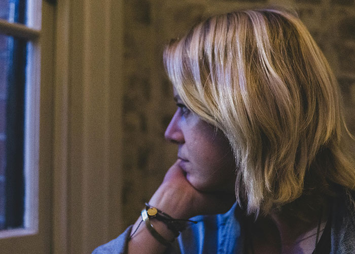 Woman with blonde hair looking out window, appearing thoughtful and worried about pregnancy and mother-in-law issues. Woman with blonde hair looking out window, appearing thoughtful and worried about pregnancy and mother-in-law issues.