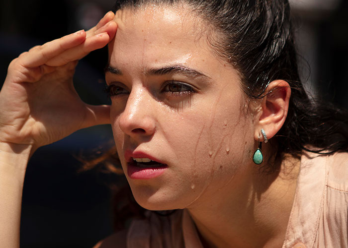 Close-up of a woman sweating and shielding her eyes, illustrating the stress of a petty revenge on an entitled dog owner.
