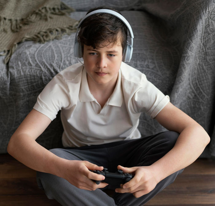 Teen boy wearing headphones and playing video games, showing frustration after years of being treated like a stranger by siblings. Teen boy wearing headphones and playing video games, showing frustration after years of being treated like a stranger by siblings.