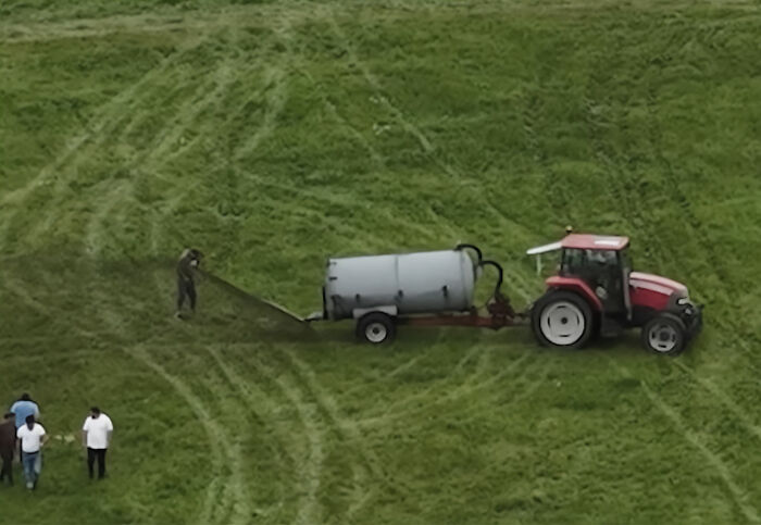 Farmer spraying manure from tractor in field with people nearby, capturing viral story and photographer&rsquo;s perspective.