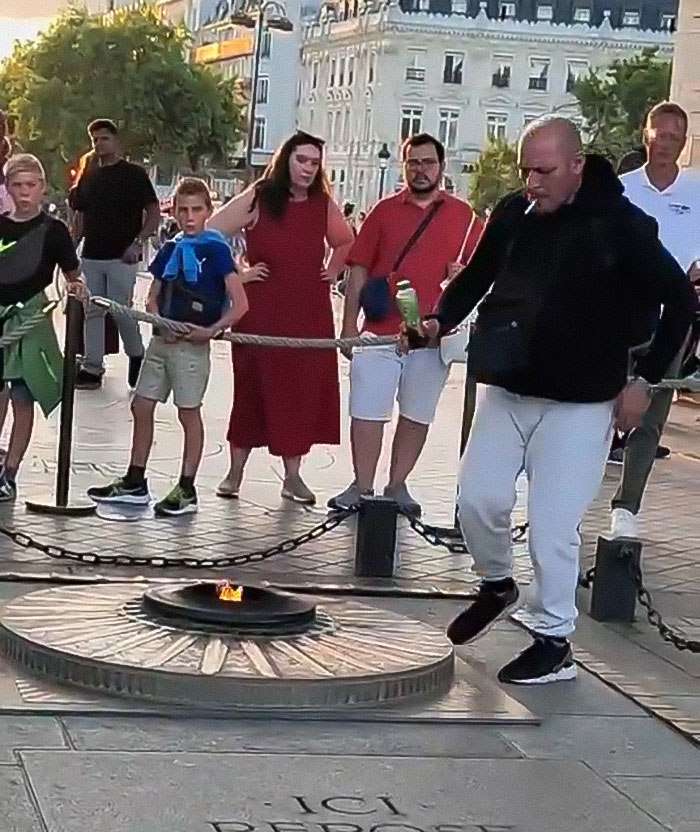 Man lighting cigarette on Tomb of Unknown Soldier flame, people watching nearby in public area. - 5