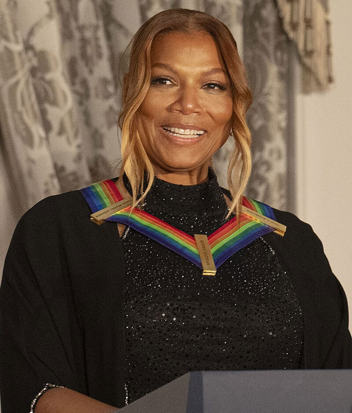 Smiling woman wearing a rainbow-colored medal necklace standing at a podium showcasing family flexes style.
