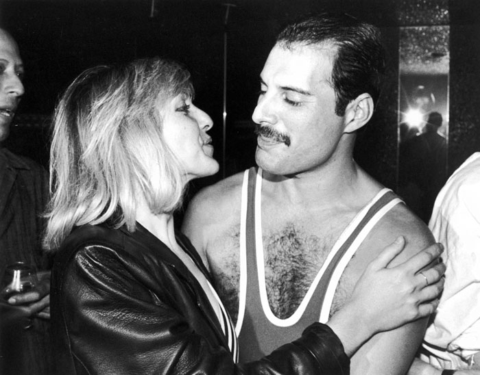 Freddie Mercury in a sleeveless top with a woman embracing him, relating to Freddie Mercury love child controversy.