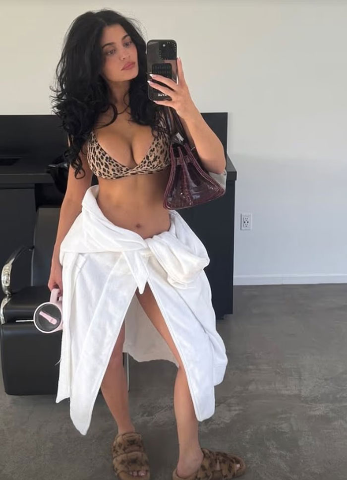 Kylie Jenner rocks risqu&eacute; leopard print outfit with white robe tied around waist in a casual indoor setting.