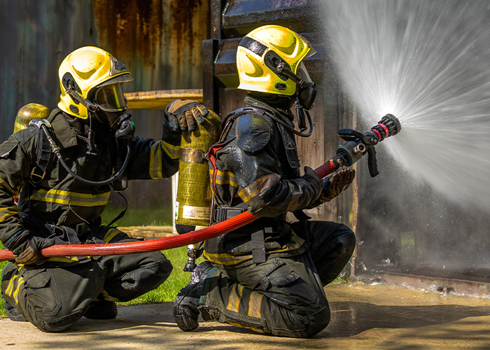 Firefighters in full gear extinguishing a house fire, highlighting common causes of house fires including accidental candle incidents.