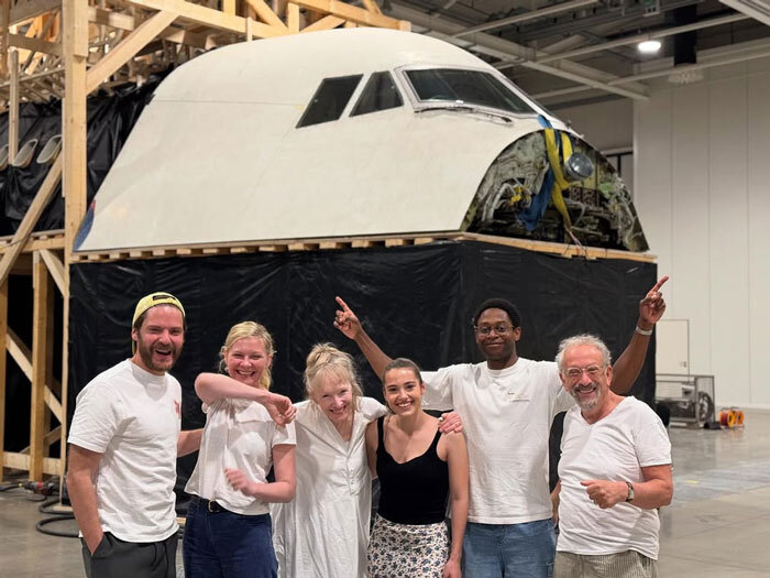 Group of six people posing smiling in front of a large airplane nose, related to Kirsten Dunst pronunciation discussion. Group of six people posing smiling in front of a large airplane nose, related to Kirsten Dunst pronunciation discussion.