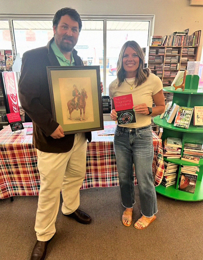 Man holding a framed painting and woman smiling in a bookstore after reading the message on the back of the painting. Man holding a framed painting and woman smiling in a bookstore after reading the message on the back of the painting.