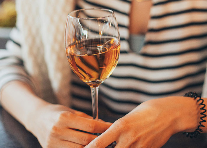 Person holding a glass of wine, illustrating risky behavior related to drive over the speed limit and illegal actions.