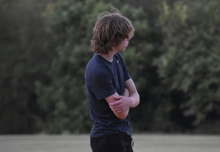 Teen boy standing outside with arms crossed, looking away, illustrating mom telling teen son to leave home regret story. - 9