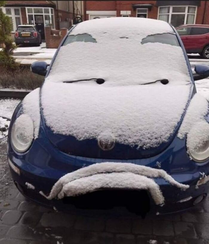 Blue car covered in snow resembling a face with eyes and a sad mouth among random objects that look like faces.