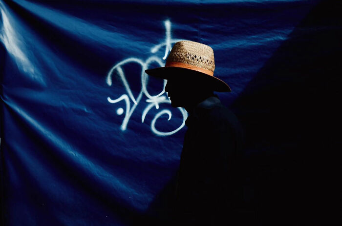 Silhouetted person wearing a straw hat against a blue wall with graffiti, a candid everyday moment from Asia.