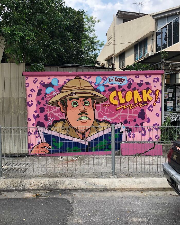 Colorful street art mural of a confused explorer with the word Cloak on an urban wall behind a metal fence.
