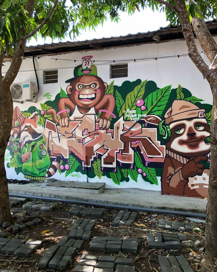 Street art mural featuring cartoon animals and vibrant graffiti with lush green leaves on an outdoor wall background.