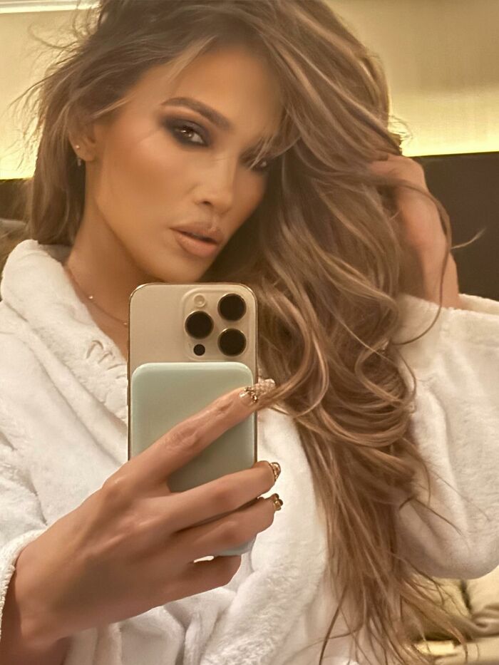 Celebrity taking a mirror selfie in a robe, showcasing glamorous makeup and styled hair, highlighting out-of-touch moments.