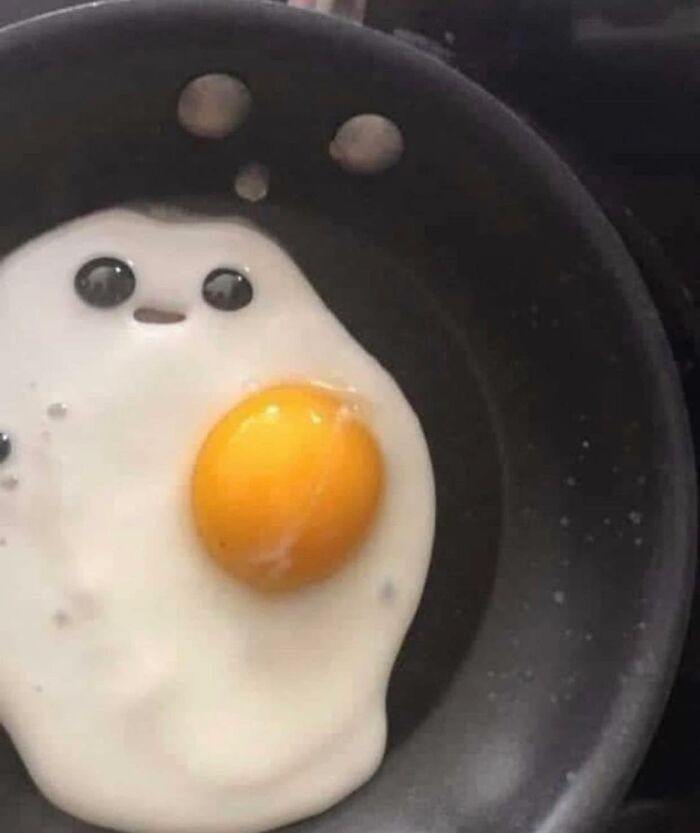 Fried egg in a pan with yolk and bubbles creating a random object that looks like faces in cooking scene.