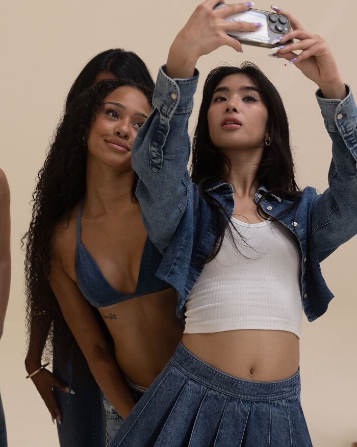 Two women wearing denim outfits, posing for a selfie in a casual Gap jeans ad setting.