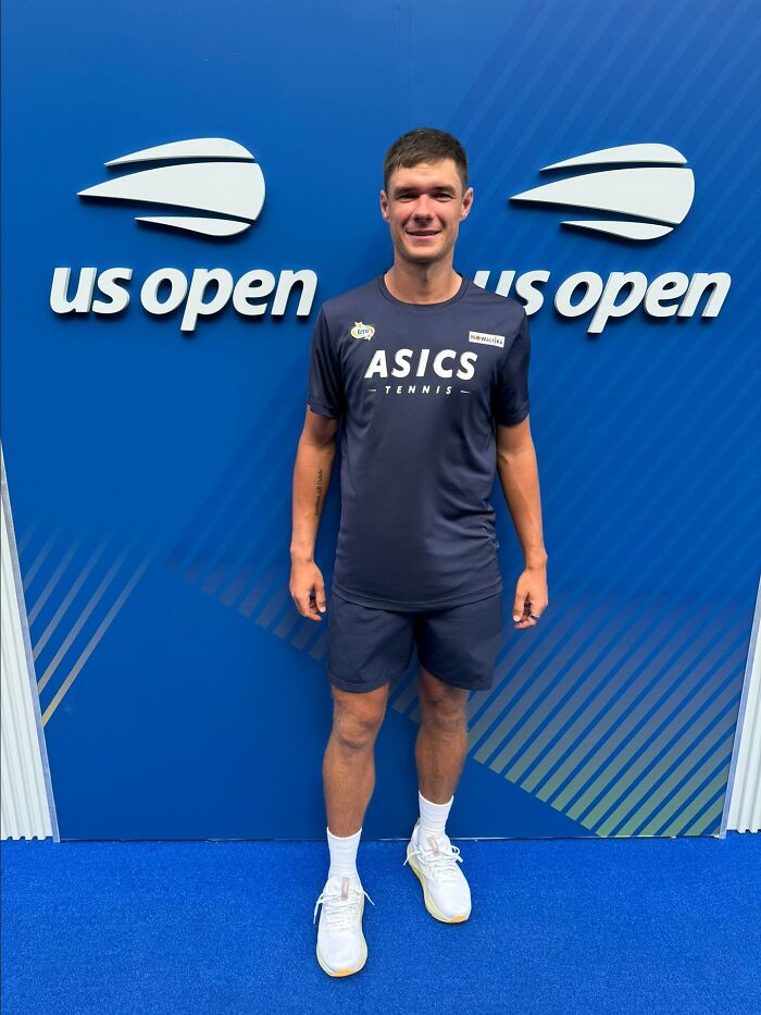 Kamil Majchrzak standing in front of US Open backdrop wearing ASICS tennis outfit, related to viral hat snatch incident.
