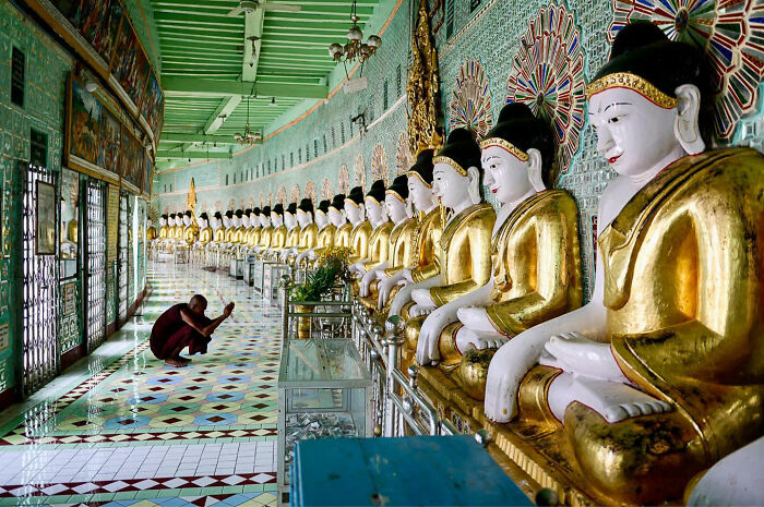 Candid everyday moment of a person praying inside an Asian temple with a row of golden Buddha statues along the wall.