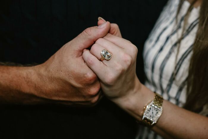 Close-up of couple holding hands showing Taylor Swift engagement ring with a large diamond in a gold setting.