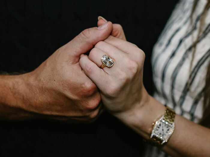 Close-up of hands with a large engagement ring, highlighting fans calling Taylor Swift's engagement a marketing stunt.
