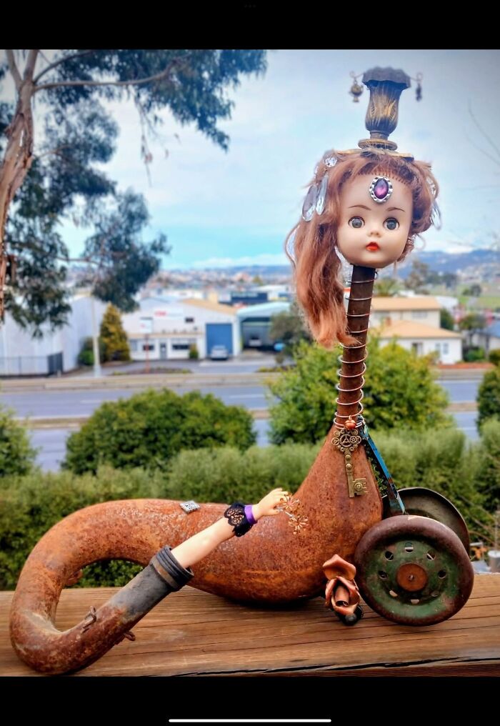 Rusty metal sculpture with a doll head and arm, adorned with jewelry, representing horrendous DIY craft shaming project.