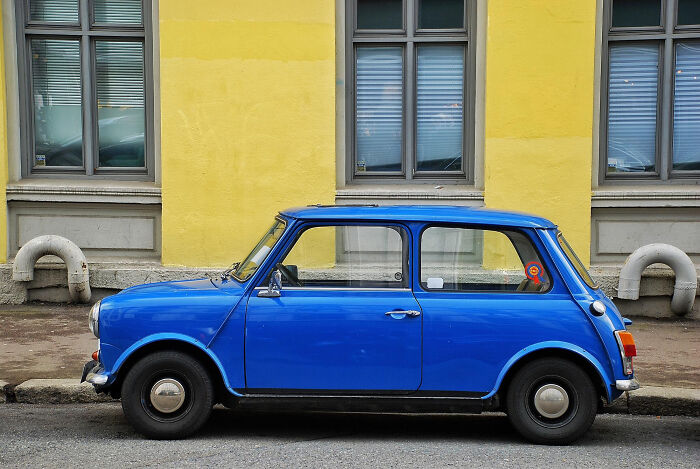 Blue vintage car parked on the street in front of a yellow building, showcasing wild confidence and school kids' creativity.