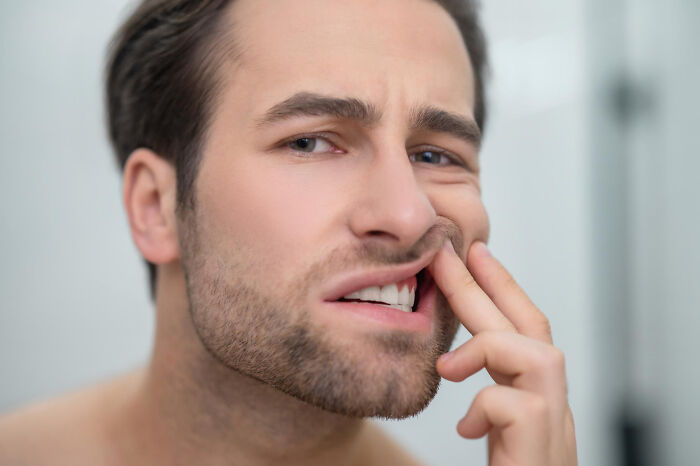 Man with stubble examining his mouth closely and pulling lip to reveal teeth, expressing discomfort or concern.