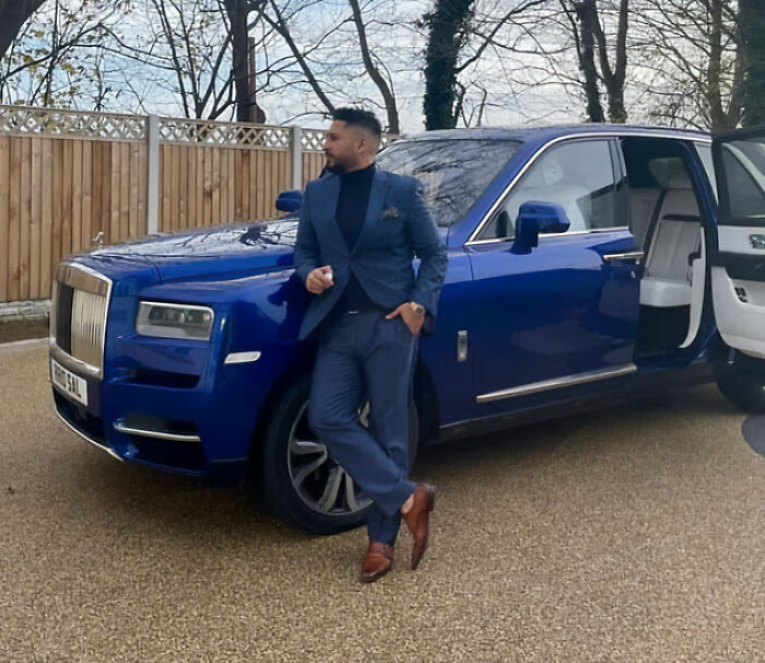 Man in a blue suit standing by a luxury blue car, reflecting on the flight attendant incident and related pain. Man in a blue suit standing by a luxury blue car, reflecting on the flight attendant incident and related pain.