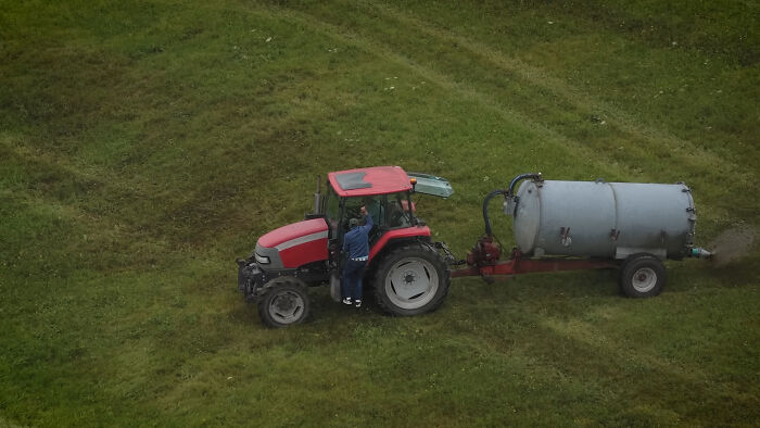 Farmer spraying manure with tractor on green field, capturing viral moment involving squatters from a photographer's viewpoint.