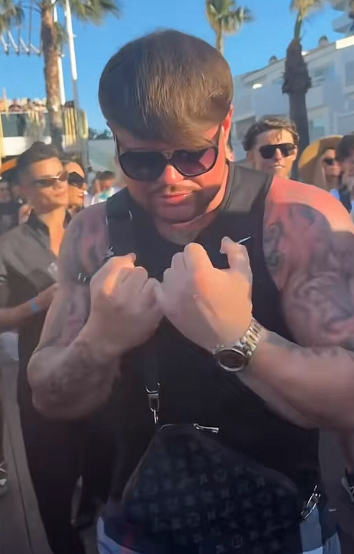 Muscular man with sunglasses and tattoos posing at a crowded outdoor party, linked to Ibiza Final Boss viral haircut meme. Muscular man with sunglasses and tattoos posing at a crowded outdoor party, linked to Ibiza Final Boss viral haircut meme.