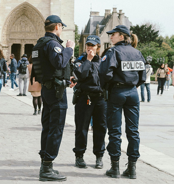 Three police officers in uniform standing and talking near a historic building about man arrested lighting cigarette on tomb