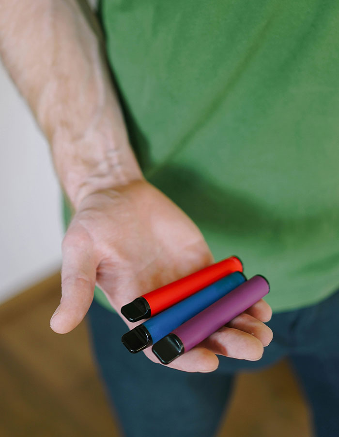 Man holding three colorful vape devices in hand, relating to vaping on plane incident with flight attendant conflict.